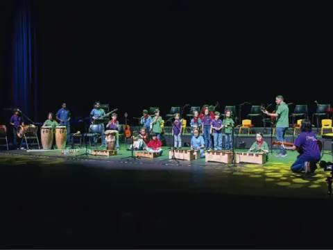 Grupo infantil de música interpretando con xilófonos y percusión en un gran escenario.