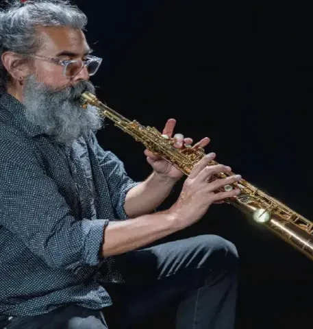Músico de barba y gafas interpretando concentrado un saxofón soprano.