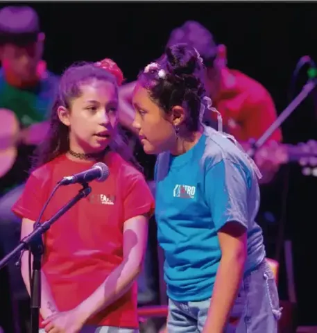 Dos niñas cantando juntas en el escenario frente a un micrófono.