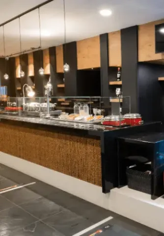 Barra de autoservicio de restaurante con recipientes de comida y lámparas colgantes.