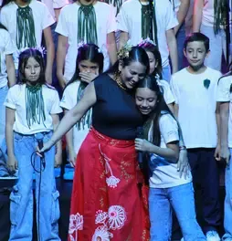 Marta Gómez abrazando sonriente a una niña del coro Cantoalegre durante la presentación.