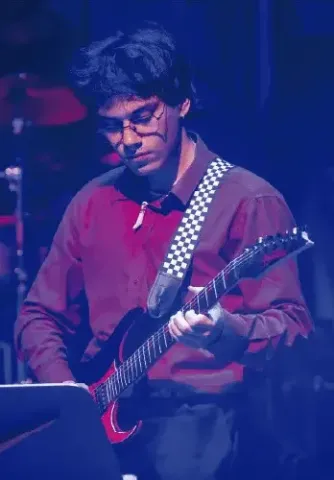 Guitarrista con gafas interpretando una guitarra eléctrica en una presentación en vivo.