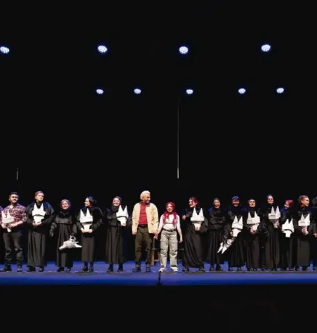 Elenco completo de una obra teatral alineado en el escenario para recibir el saludo final.