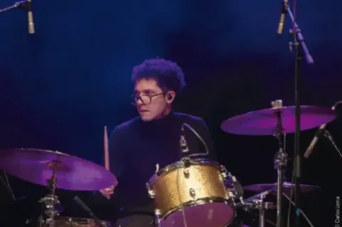 Baterista con gafas tocando en el escenario bajo iluminación azul.