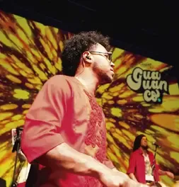 Percusionista tocando en el escenario con un fondo visual colorido de la presentación.