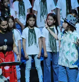 Marta Gómez y un niño con sombrero interactuando en el escenario junto al coro Cantoalegre.
