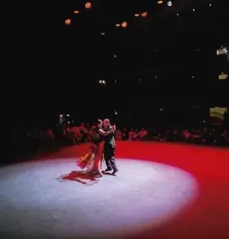 Pareja de tango ejecutando un movimiento destacado bajo un reflector en el escenario.