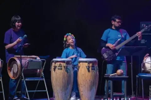 Niña tocando congas en vivo acompañada por un bajista y percusionista.