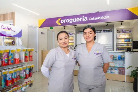 Dos mujeres con uniforme de Droguería Colsubsidio sonríen en el punto de servicio