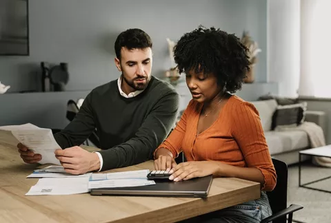 Pareja organiza sus finanzas en casa con una libreta y una calculadora sobre la mesa, gracias al webinar PerteneSer